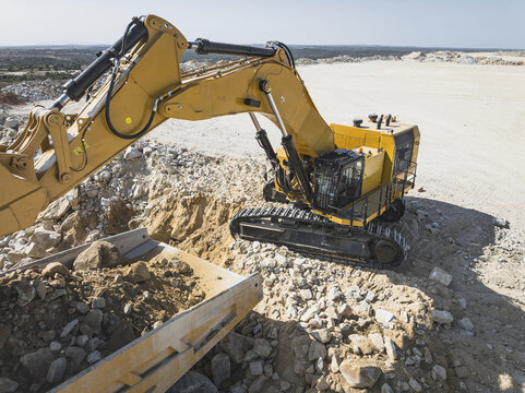 Santa Lucia de Gordon, Spain: View of a large yellow excavator parked in a quarry under a clear blue sky.