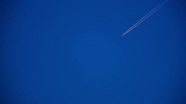 High Altitude Aircraft Leaving Vapor Trail in Sky. Airplane Crossing Blue Sky with Long White Trail. Jet Stream Trail Behind Airplane in Clear Sky. Minimal Sky Scene Plane and Contrail Motion. 