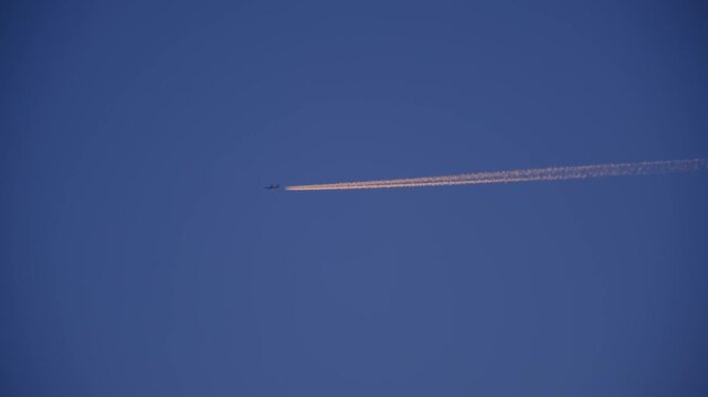 High Altitude Aircraft Leaving Vapor Trail in Sky. Airplane Crossing Blue Sky with Long White Trail. Jet Stream Trail Behind Airplane in Clear Sky. Minimal Sky Scene Plane and Contrail Motion. 