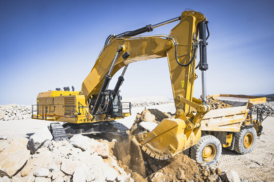 Santa Lucia de Gordon, Spain: View of a large yellow excavator parked in a quarry under a clear blue sky.