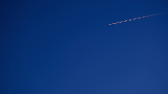High Altitude Aircraft Leaving Vapor Trail in Sky. Airplane Crossing Blue Sky with Long White Trail. Jet Stream Trail Behind Airplane in Clear Sky. Minimal Sky Scene Plane and Contrail Motion. 