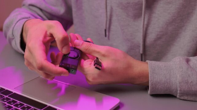 Hands carefully inspect compact sound card setup under purple lighting. Technician examines external audio device while preparing cables in softly lit environment
