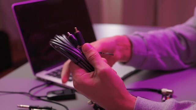 Preparing audio setup with focus on connection and ambient lighting. Attaching audio cable to laptop emphasizing precise finger placement and purple studio illumination