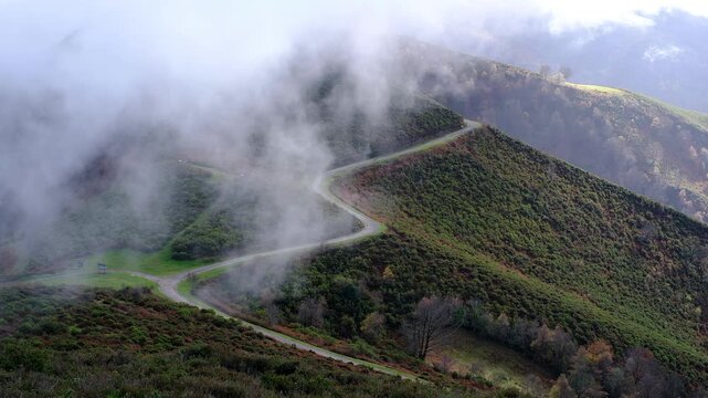 Winding mountain road disappearing into thick white fog in the lush green hills of San Martin del Rey Aurelio, Asturias. 
