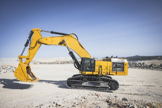 Santa Lucia de Gordon, Spain: View of a large yellow excavator parked in a quarry under a clear blue sky.