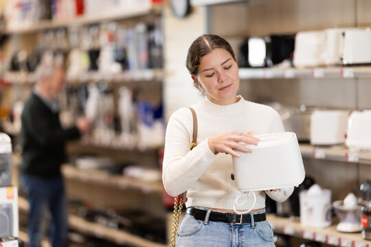 Positive young woman choosing toaster in hypermarket and smiling