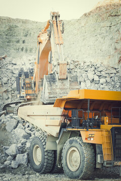 Santa Lucia de Gordon, Spain: View of a large yellow excavator loading grey rocks into a massive dump truck in an open-pit mine.