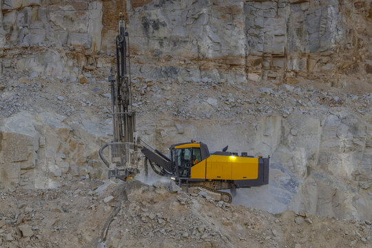 Santa Lucia de Gordon, Spain: View of a large yellow excavator loading grey rocks into a massive dump truck in an open-pit mine.