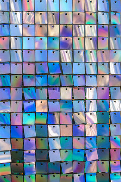 Iridescent sequin wall shows rows of square discs pinned in grid with rainbow reflections, mosaic pattern, metallic shine. Sequin pattern, natural colorful background