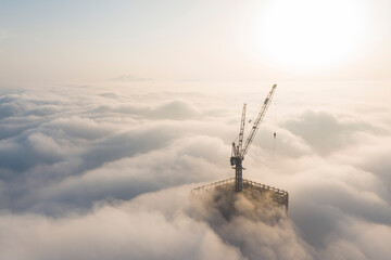 Silhouette of a high-rise construction tower crane piercing through a thick sea of advection fog during a beautiful golden sunrise in Wuhan, China. Urban city development rising above the clouds. © 晨啸 周