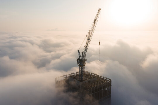 Silhouette of a high-rise construction tower crane piercing through a thick sea of advection fog during a beautiful golden sunrise in Wuhan, China. Urban city development rising above the clouds.