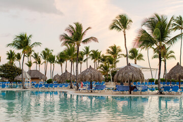 Fototapeta premium Tropical resort pool area with palm trees and sun loungers at sunset