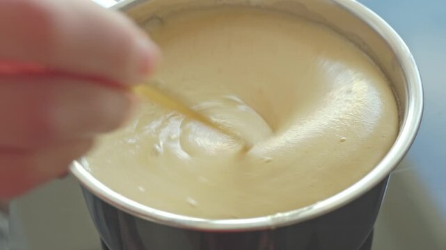 Spoon stirs creamy mixture in metal pot during cooking preparation. Concept of homemade recipe and food preparation