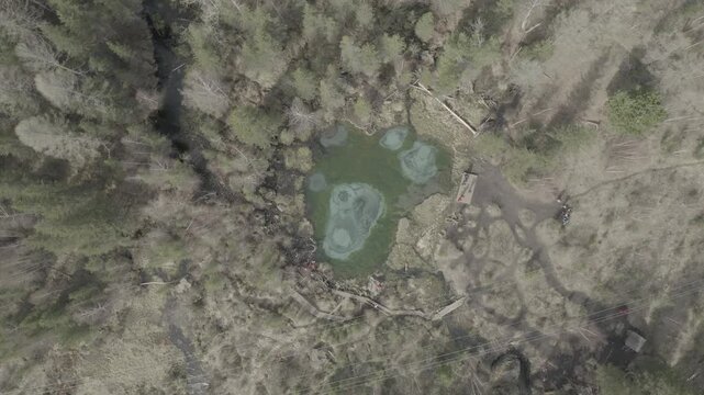 Aerial perspective showcasing icy woodland pond landscape. Cinematic top down view emphasizes isolated turquoise water body amidst winter woodland and marsh environments