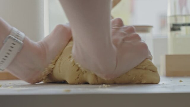 Hands knead dough on kitchen surface during baking preparation. Concept of homemade cooking and pastry recipe