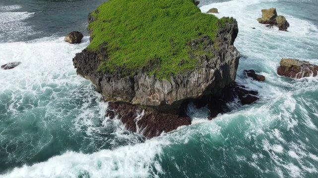 Aerial view of a lush green rocky islet surrounded by powerful ocean waves crashing dramatically against the cliffs.