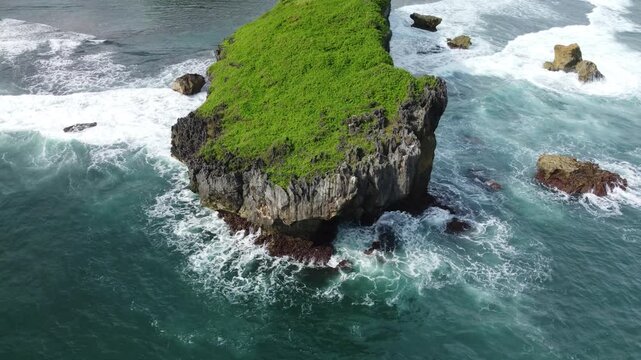 Aerial view of a lush green rocky islet surrounded by powerful ocean waves crashing dramatically against the cliffs.