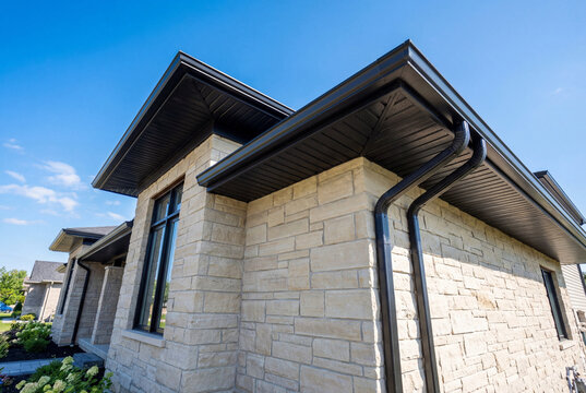 Exterior detail of a modern house with black gutters and light stone siding under a blue sky