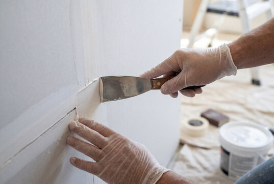 Construction worker wearing protective gloves applies white joint compound to a drywall seam