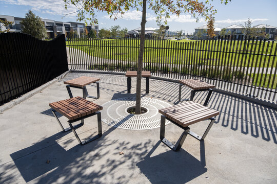 Contemporary benches arranged around a young tree with a decorative circular grate.&nbsp;Modern outdoor seating area in a new suburban parkland in a new estate. Melbourne, Australia