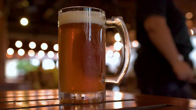 Close up of two cold glasses of draft beer on wooden table in outdoor cafe with bokeh background lights.