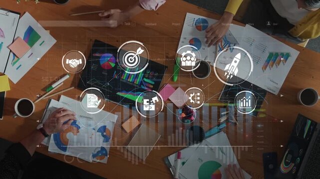Aerial view of a collaborative business meeting showcasing teamwork and innovation with charts and data analysis on a wooden table surrounded by professionals. Raster