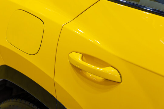 A yellow car door handle and gas cap on the body of a modern passenger vehicle. Side view