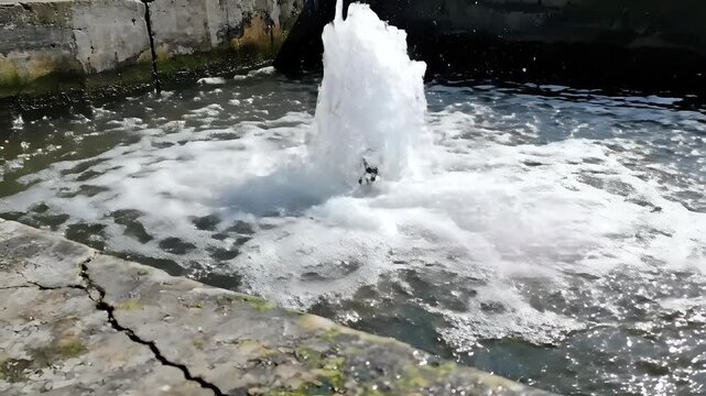 Powerful water geyser erupting from cracked concrete surface.