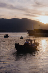 Obraz premium Fishermen on a boat head out to sea at sunrise in Quy Nhon, Binh Dinh, Vietnam. The sun rises behind the mountains, casting a golden glow on the water.