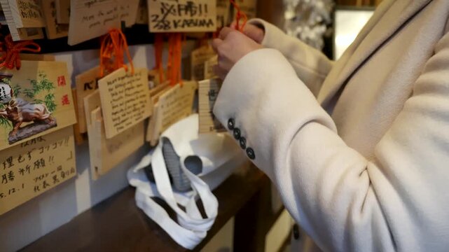 Woman hanging wooden ema prayer plaque at japanese shrine for good luck and wishes.