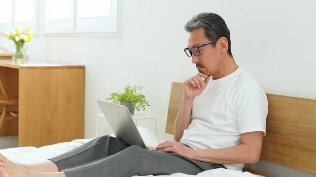 ベッドの上でパソコンを使う中高年の男性
