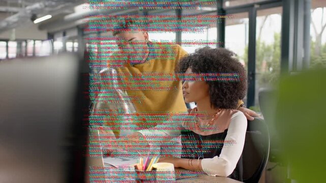 Woman at laptop pointing, man leaning and causing code overlay obscuring screen while fixing code