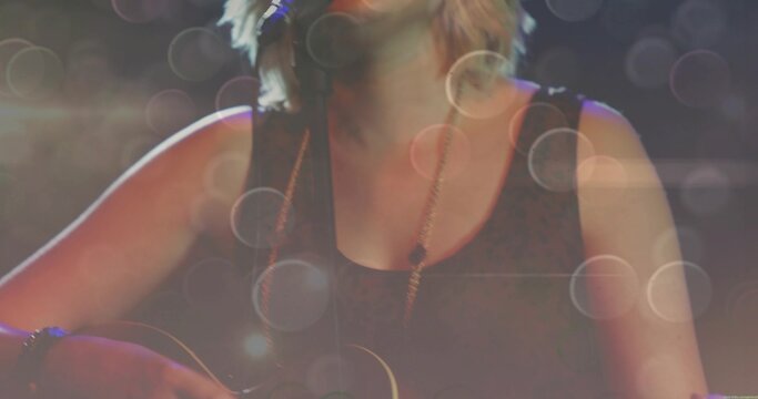 Singing teen performer playing guitar into mic onstage wearing sleeveless black top and necklace