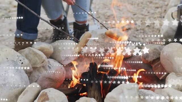 Two campers holding hotdogs over flames rotating skewers browning food star overlay obscuring frame