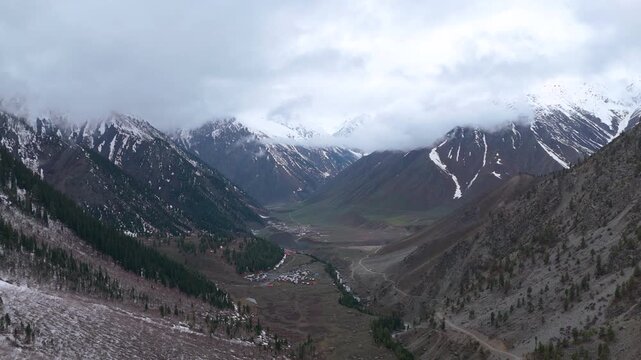 Drone Trucking Clip of a Remote Mountain Village in a Cloud-Shrouded Alpine Valley, Burzil Nala River Flowing Through a Snowy Himalayan Pass