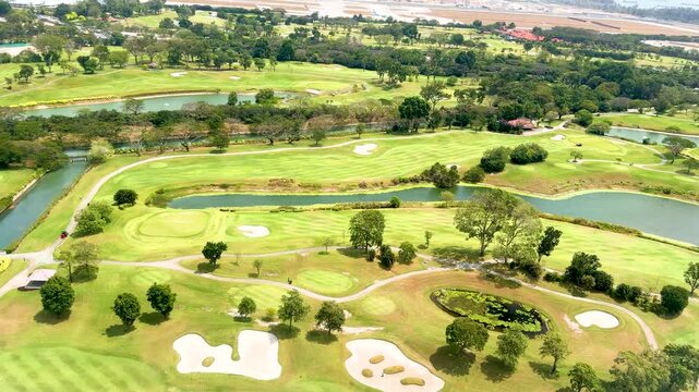 Cinematic aerial view of luxury golf course with green fairways sand bunkers and water hazards under bright sunlight.
