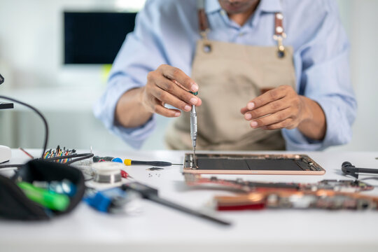 Technician repairing broken tablet using screwdriver in electronics repair shop