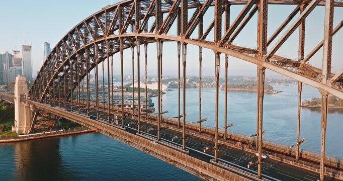 Sydney Harbour Bridge spanning bay, carrying cars and trains across water with the city skyline beneath a clear blue sky on sunny day. Modern Australia cityscape architecture. Aerial view static shot