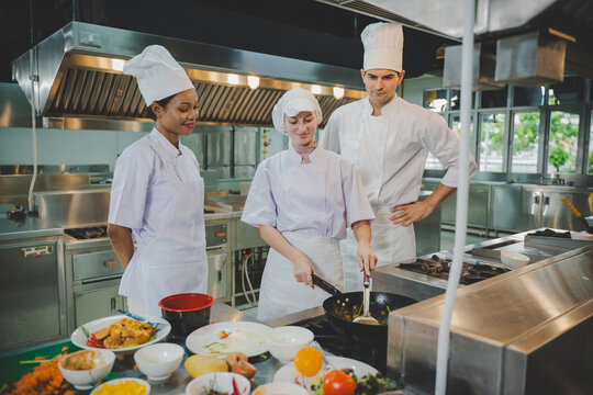 Culinary instructor teaching students wok cooking techniques in professional training kitchen