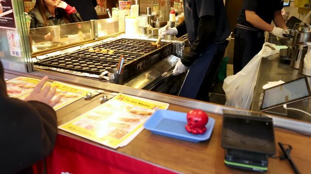 A motion of street food vendor cooking takoyaki octopus balls, a popular japanese snack, in a busy market setting.