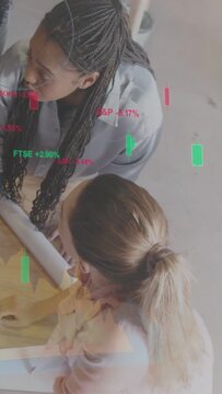 Vertical video: Two women leaning over plans, camera revealing market overlay guiding review