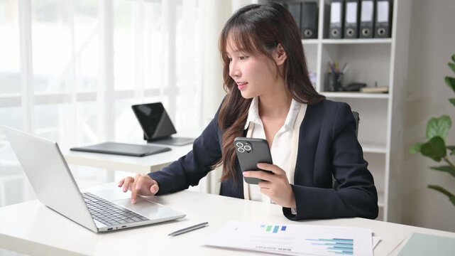 Businesswoman working with smartphone and laptop at office desk