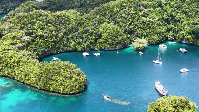 Aerial view of luxury yachts anchored in crystal clear blue lagoon surrounded by tropical limestone islands of Palau.