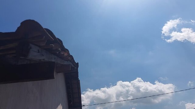 Traditional tiled roof edge under a bright blue sky with white clouds captured on a clear spring afternoon in year 2026
