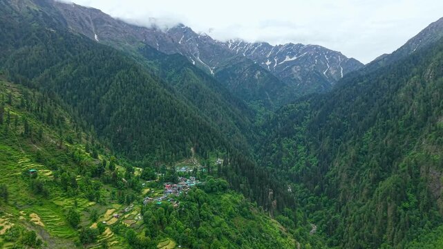 Grahan village with colorful rooftops, terraced farmland, and dense pine forests set within a deep Himalayan valley near Parvati Valley, Himachal Pradesh, India. Wide aerial view