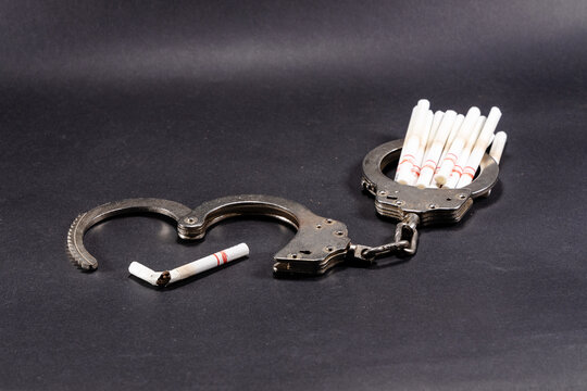 handcuffs with a cigarette on black background. Concept of addiction