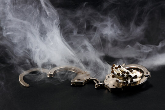 handcuffs with a cigarette on black background. Concept of addiction.