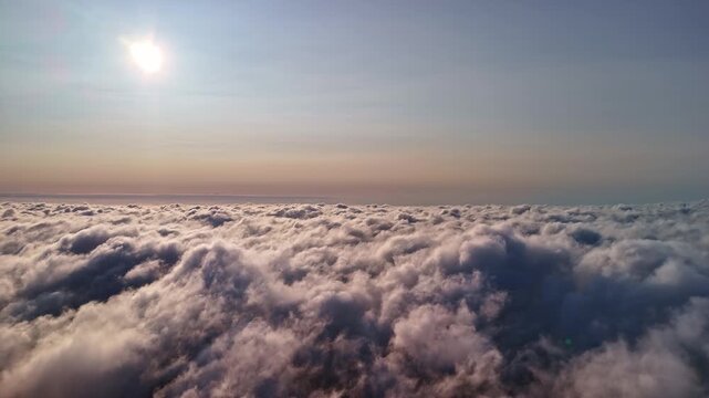 Aerial view above a vast cloud layer in soft sunlight, capturing a peaceful skyscape with glowing mist and endless billowing clouds at high altitude.