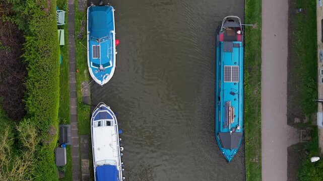 A top-down forward drone shot follows a duck swimming along the Leeds and Liverpool Canal in Skipton, with colourful moored narrowboats and canal boats on both banks. Spring footage.