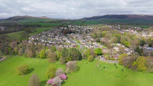 A forward drone flight over Aireville Park, Skipton, North Yorkshire, reveals the Rockwood Drive estate nestled among spring trees, with surrounding fells and green fields beyond.